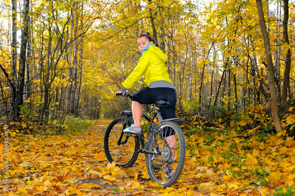 Girl with a bicycle on an alley in autumn forest