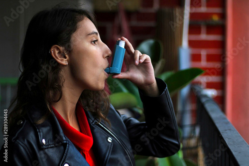 Health and medicine - Young girl using blue asthma inhaler to prevent an asthma attack.