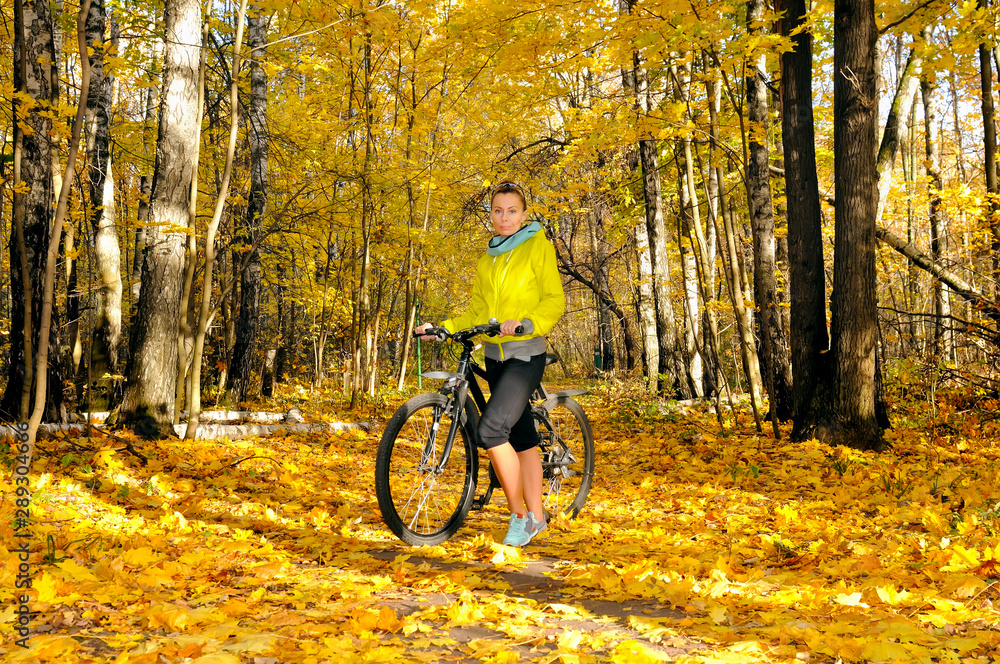 Girl with a bicycle on an alley in autumn forest