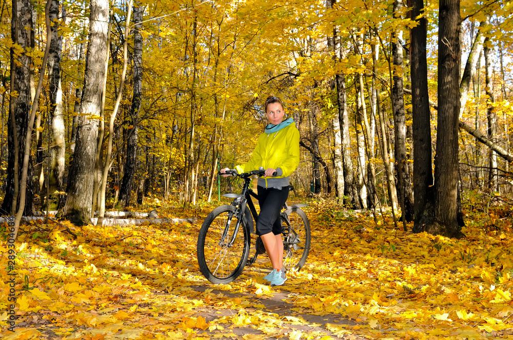 Girl with a bicycle on an alley in autumn forest