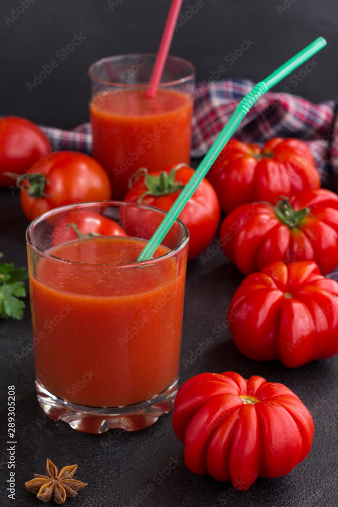 Tomato juice in a glass among tomatoes on a black background. Checkered napkin Tomato juice in a glass among tomatoes on a black background. Checkered napkin