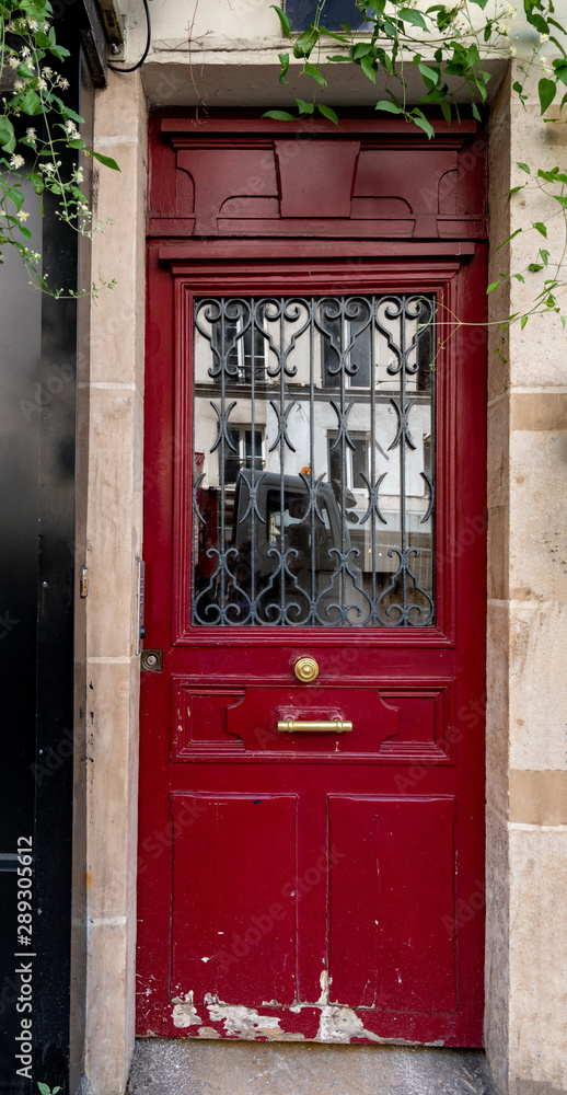 Red wooden door. Red painted wooden door with reflective glass window protected by ornate metal gratings. Antique building entrance in Paris France. Architecture details. Travel Europe.
