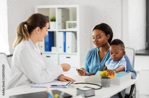 medicine, healthcare and pediatry concept - caucasian doctor giving prescription to african american mother with baby son at clinic