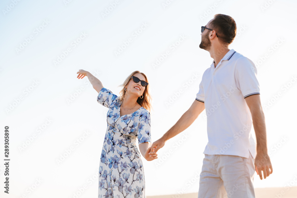 Photo of nice woman pointing finger at sky and young man looking at sky while walking on beach Photo of nice woman pointing finger at sky and young man looking at sky while walking on beach