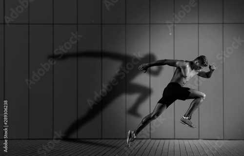 Athletic man sprinter running on dark wall background photo