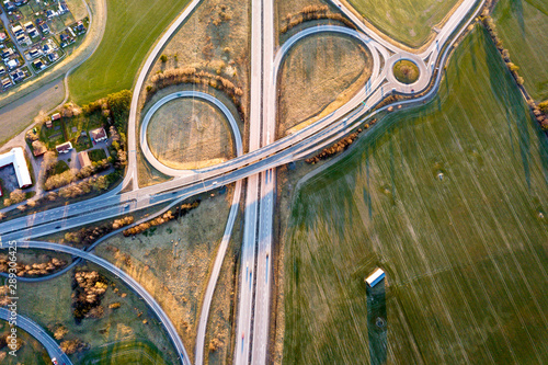 Aerial top view of modern highway road intersection, house roofs on spring green field background. Drone photography.