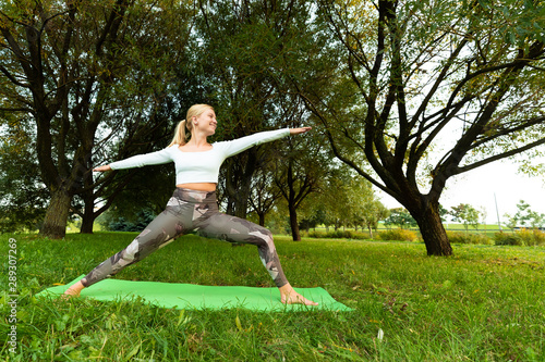 Blonde in a white t-shirt and sports leggings doing yoga on a rug in the park © makedonski2015