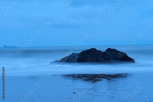 large rock in the middle of the beach, sea water in long exposure
