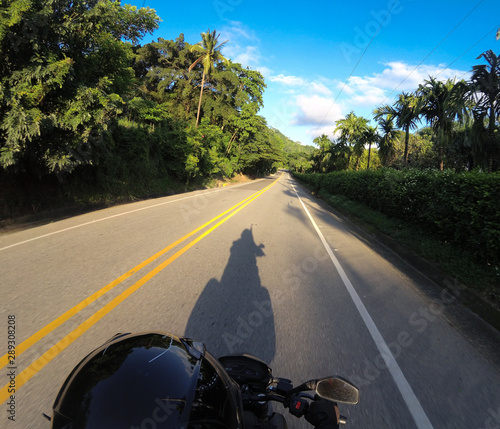 sombra de moto en carretera rodeada por vegetación verde y cielo azul