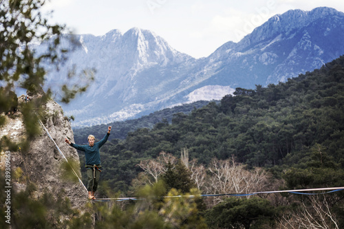 A man is walking along a stretched sling. Highline in the mountains. Man catches balance. Performance of a tightrope walker in nature. Highliner on the background of the mountains.