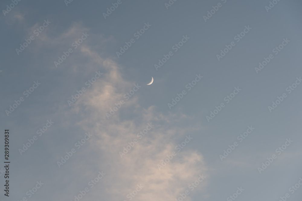 a new moon in the dusk sky and white clouds