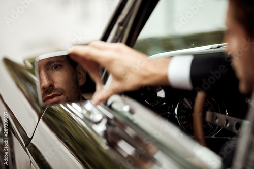 Young handsome man driving a car and looking at mirror