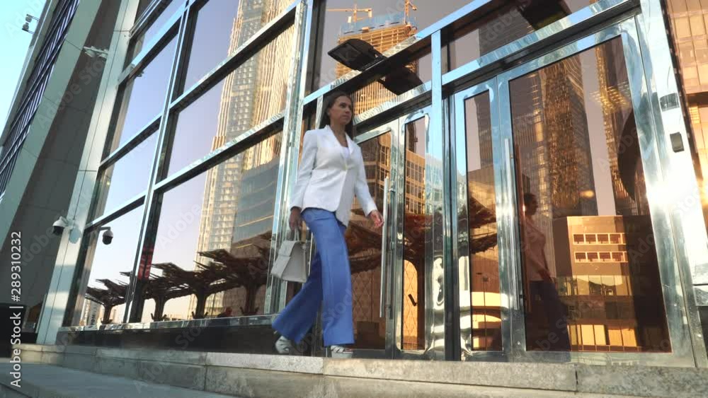 A beautiful girl goes to work along modern buildings. She is wearing a business suit and a stylish bag in her hand. A beautiful girl goes to work along modern buildings. She is wearing a business suit and a stylish bag in her hand.