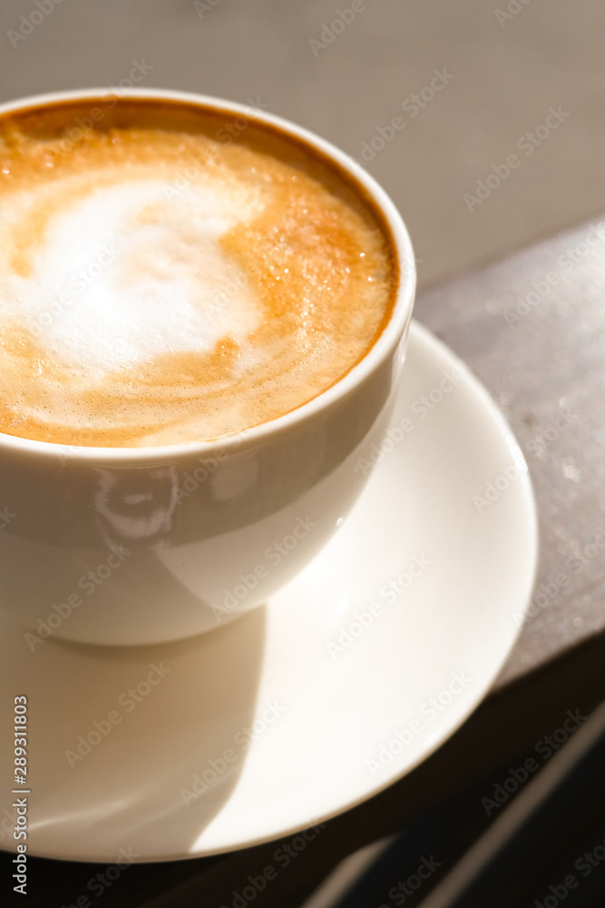 Cappuccino in white cup on sunlight at cafe. Copyspace. Bewerages, coffee lovers and morning menu concept. Brown background Cappuccino in white cup on sunlight at cafe. Copyspace. Bewerages, coffee lovers and morning menu concept. Brown background