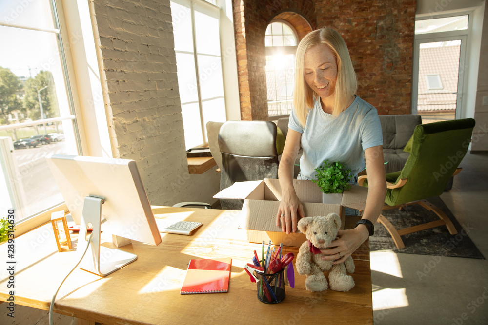 A young businesswoman moving in the office, getting new work place. Young caucasian female office worker equips new cabinet after promotion. Looks happy. Business, lifestyle, new life concept. A young businesswoman moving in the office, getting new work place. Young caucasian female office worker equips new cabinet after promotion. Looks happy. Business, lifestyle, new life concept.