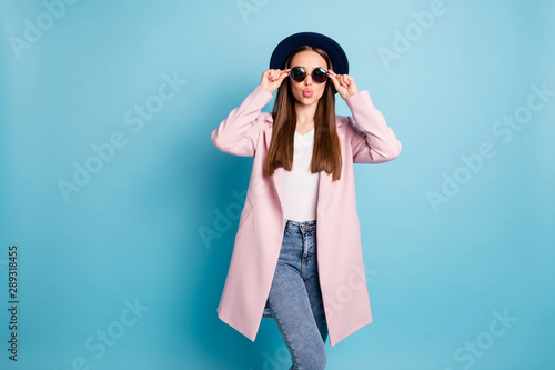 Portrait of pretty girl in eyeglasses eyewear have date with boyfriend send him air kisses wear pink topcoat denim jeans isolated over blue background