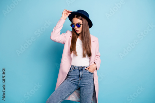Portrait of charming stylish lady posing showing her fashionable retro outfit having free time wearing pink topcoat denim jeans isolated over blue background