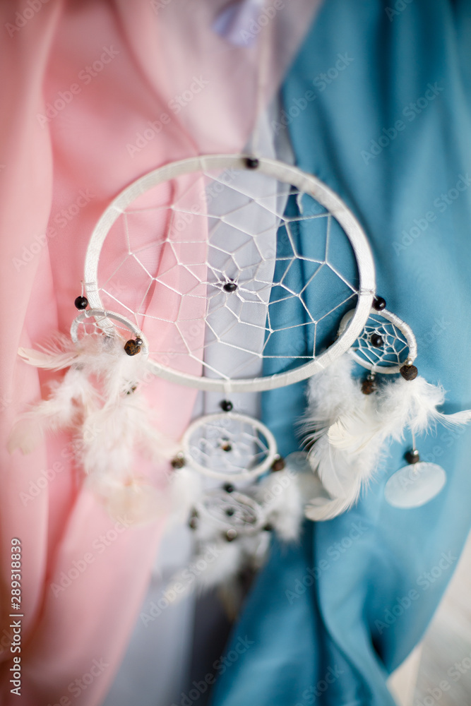 white dreamcatcher hanging on the background of colored fabric white dreamcatcher hanging on the background of colored fabric