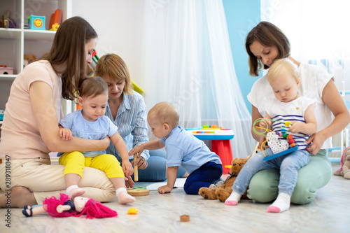 Friends with toddlers playing on the floor in play room or nursery
