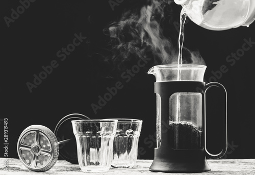 Coffee is poured into a cup from French press coffee maker , On the  old wood table and black background, Natural light, Selcetive focus, Vintage style. photo