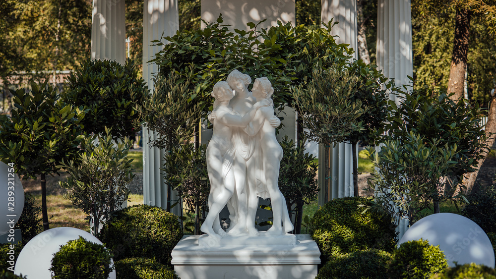 Obraz premium A beautiful white sculpture on the background of green trees in the park.