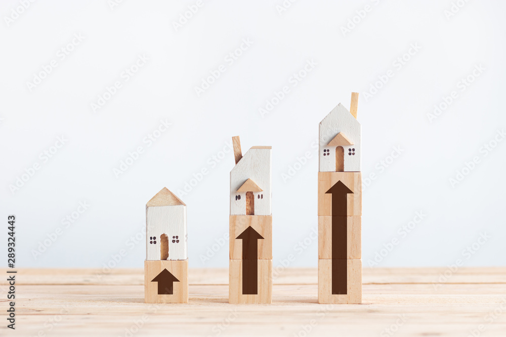 Miniature white house on wooden block with growth arrow sign in property investment concept