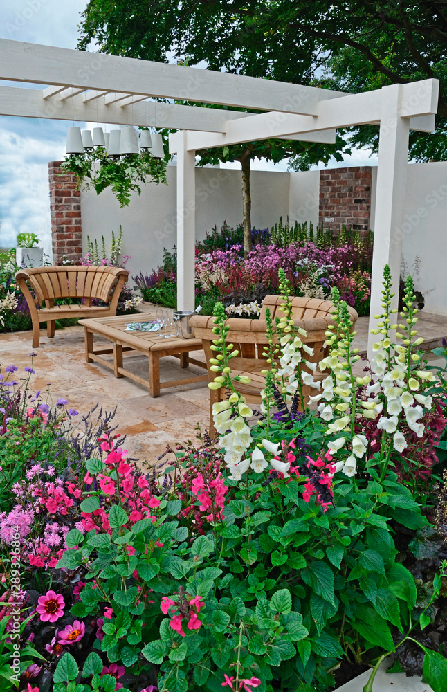 Obraz premium A contemporary garden with terraced area and stylish wooden furniture surrounded by colourful flowering borders