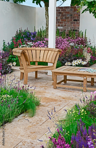 A contemporary garden with terraced area and stylish wooden furniture surrounded by colourful flowering borders © Garden Guru