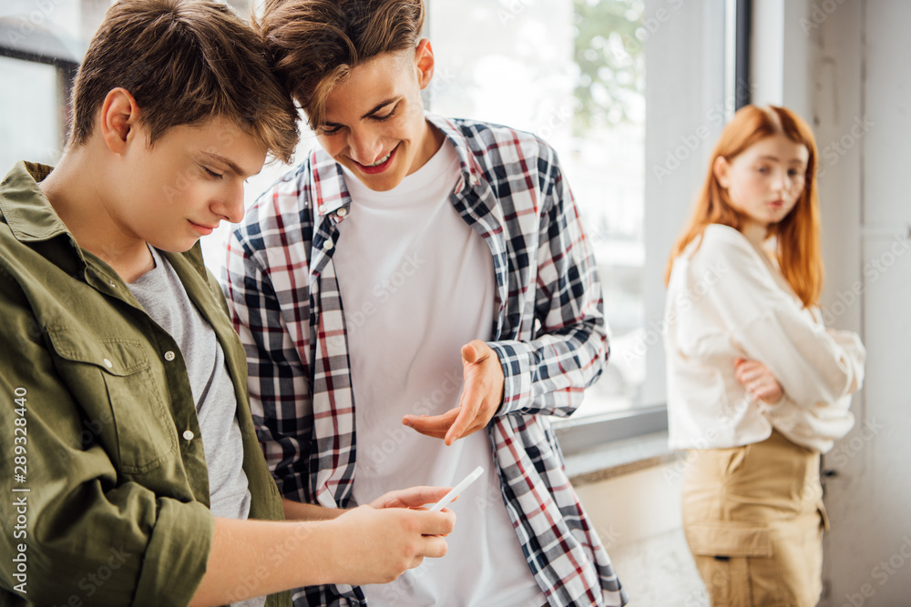 two happy teenagers smiling while using smartphone in school two happy teenagers smiling while using smartphone in school