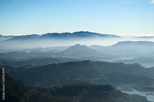 Mountain range landscape with fresh morning colors. View from Sri Pada peak (Adam's Peak) to the valley in fog and Maskeliya reservoir..Soft blue color gradients. Tranquility and freshness. Sri Lanka.