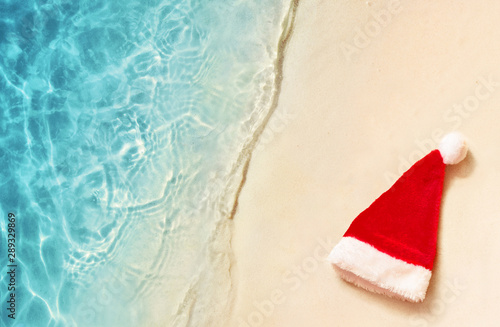 Christmas holidays concept. Top view of santa claus hat on summer sand beach.