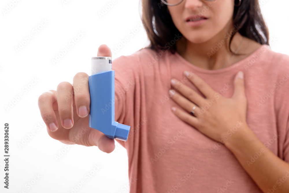 Young caucasian brunette girl with pink shirt suffers from asthma inhaling showing an inhaler. isolated in white background. Young caucasian brunette girl with pink shirt suffers from asthma inhaling showing an inhaler. isolated in white background.