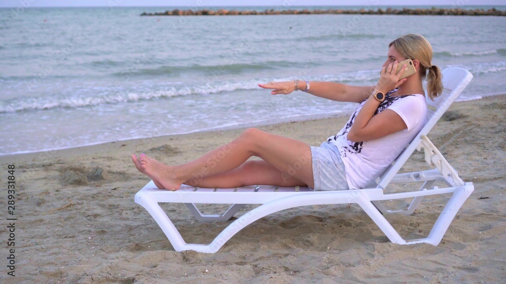 A girl is relaxing on a deck chair by the sea among the waves rolling on the shore. Holding the phone in his hands. Notices something unusual and screams ecstatically A girl is relaxing on a deck chair by the sea among the waves rolling on the shore. Holding the phone in his hands. Notices something unusual and screams ecstatically