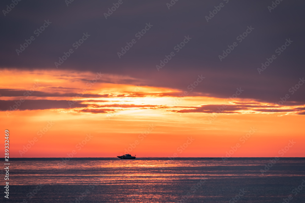 A motor boat swims quickly across the sea against a beautiful red sunset.