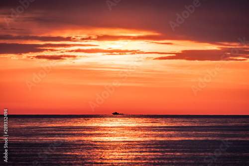 A motor boat swims quickly across the sea against a beautiful red sunset.