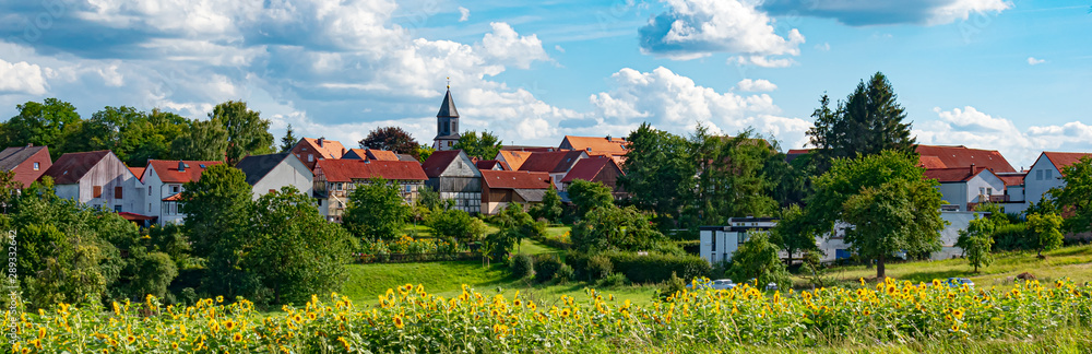 Landscape, Germany, Hesse - A blooming sunflower field with a view of Beltershausen-Frauenberg of the municipality Ebsdorfergrund. On a day with cumulus clouds in the sky in August.