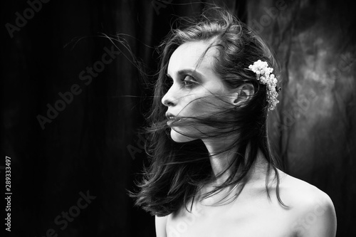 A beautiful slim girl with naked shoulders and fashionable red makeup, wearing jewelry in her hair, sensually poses while the wind blows her hair. Close Up monochrome black and white photo.
