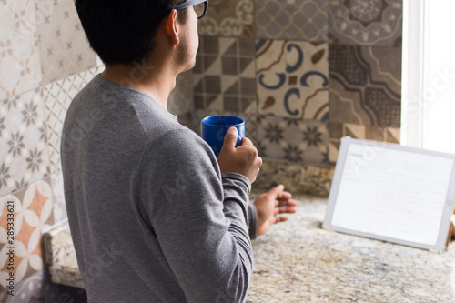 An Unrecognizable man drinks coffee and works on a tablet at home