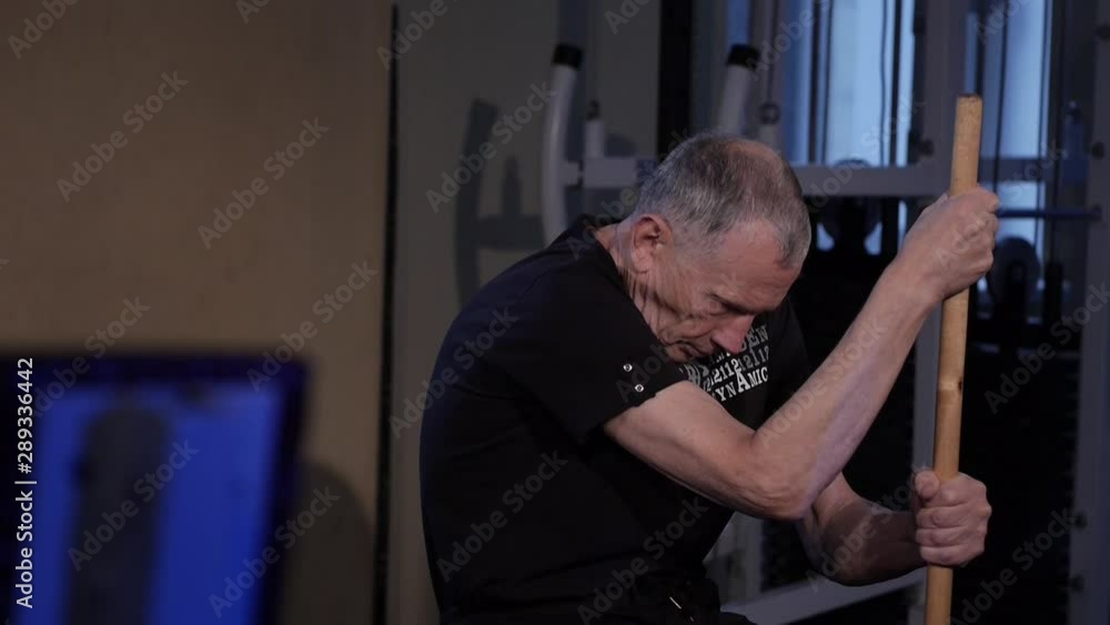 isometric exercise with a stick.an elderly man holds a stick vertically in front of him in a sitting position.Copy space.glide cam footage.side view isometric exercise with a stick.an elderly man holds a stick vertically in front of him in a sitting position.Copy space.glide cam footage.side view