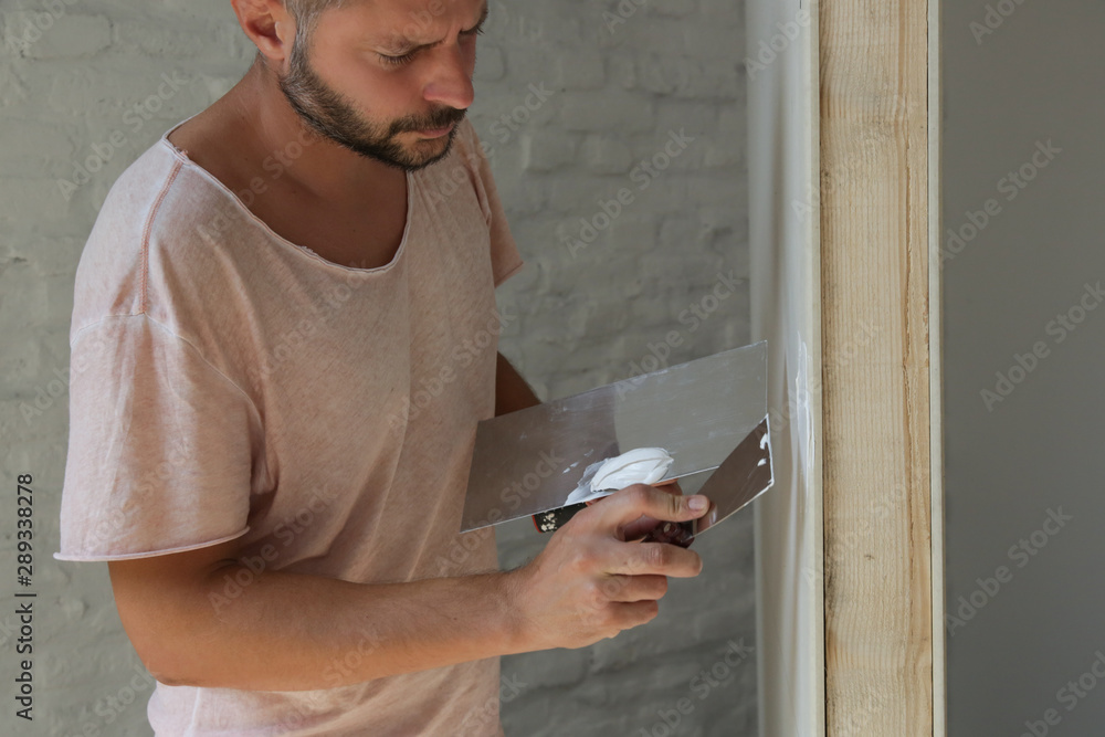 Fototapeta premium Man plastering wall with putty-knife. Fixing wall surface and preparation for painting. DIY housing improvement project.