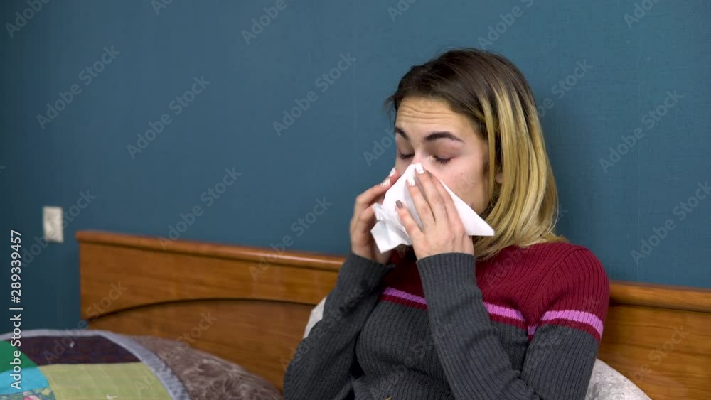 A young woman sneezes and blows her nose in a napkin. The girl is sick lying on the bed. Closeup