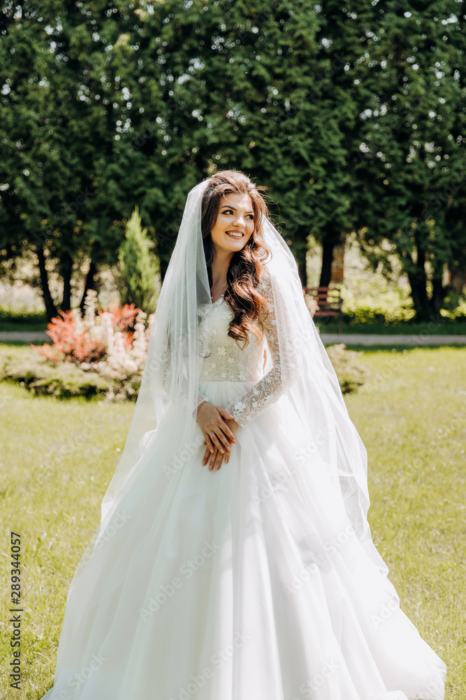 Charming bride in a white dress stands in the park