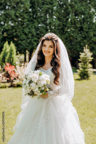 Charming bride in a white dress stands in the park