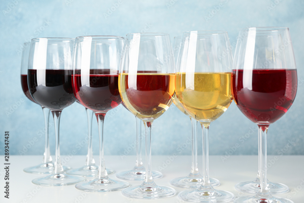 Glasses with different wine on white table against light blue background Glasses with different wine on white table against light blue background