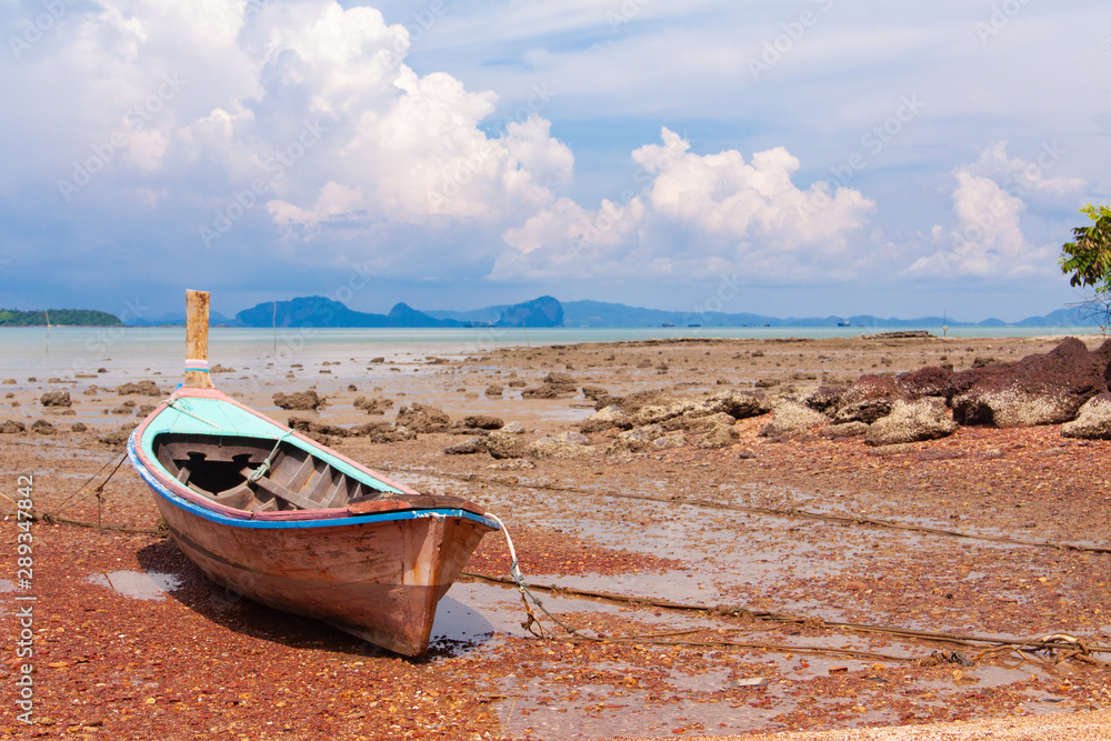 Traditional Thai longtail boat on the sand beach at the low tide. Sea view with islands on horizon and clouds in the sky. Traditional Thai longtail boat on the sand beach at the low tide. Sea view with islands on horizon and clouds in the sky.