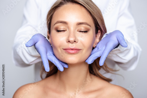 Close up portrait of young blonde woman with cosmetologyst hands in a gloves. Preparation for operation or procedure. Perfect skin, spa and care photo