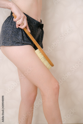 Woman makes massage legs with wooden soft massage brush for body and legs.