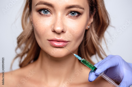 Close up portrait of blonde woman with cosmetologist hands near her face. Procedure in salon, spa and care