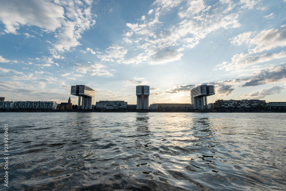 symmetric panorama skyline view of the rhine shore in cologne with water in the foreground and crane houses  in the back on a sunny day