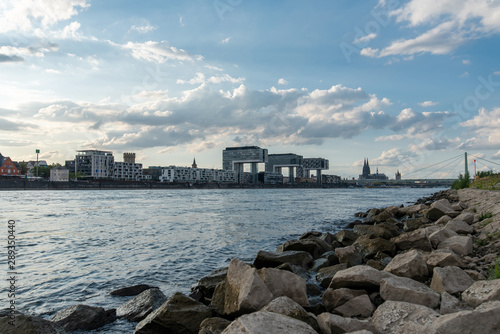 panoramic skyline view of the rhine shore in cologne with rocks in the foreground and crane houses with cathedral in the back on a sunny summer day